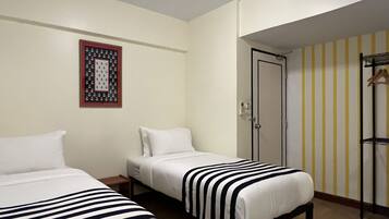 A hotel room with two beds, a framed picture on the wall, a door with a striped wallpaper, and a coat rack.
