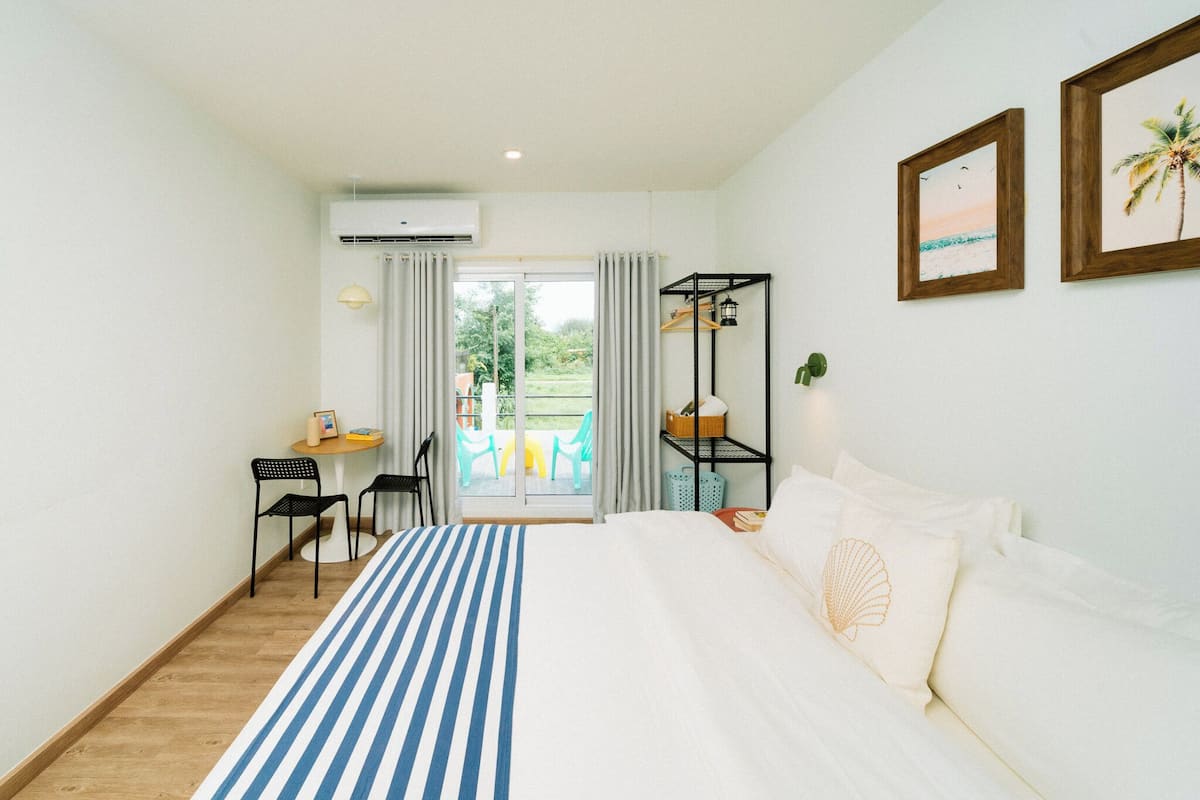 Habitación de hotel con cama, escritorio, silla, estante y vistas al exterior.