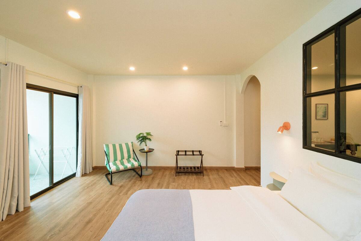 Habitación de hotel con una cama grande, una mesita con una planta, una silla y una ventana con cortinas.