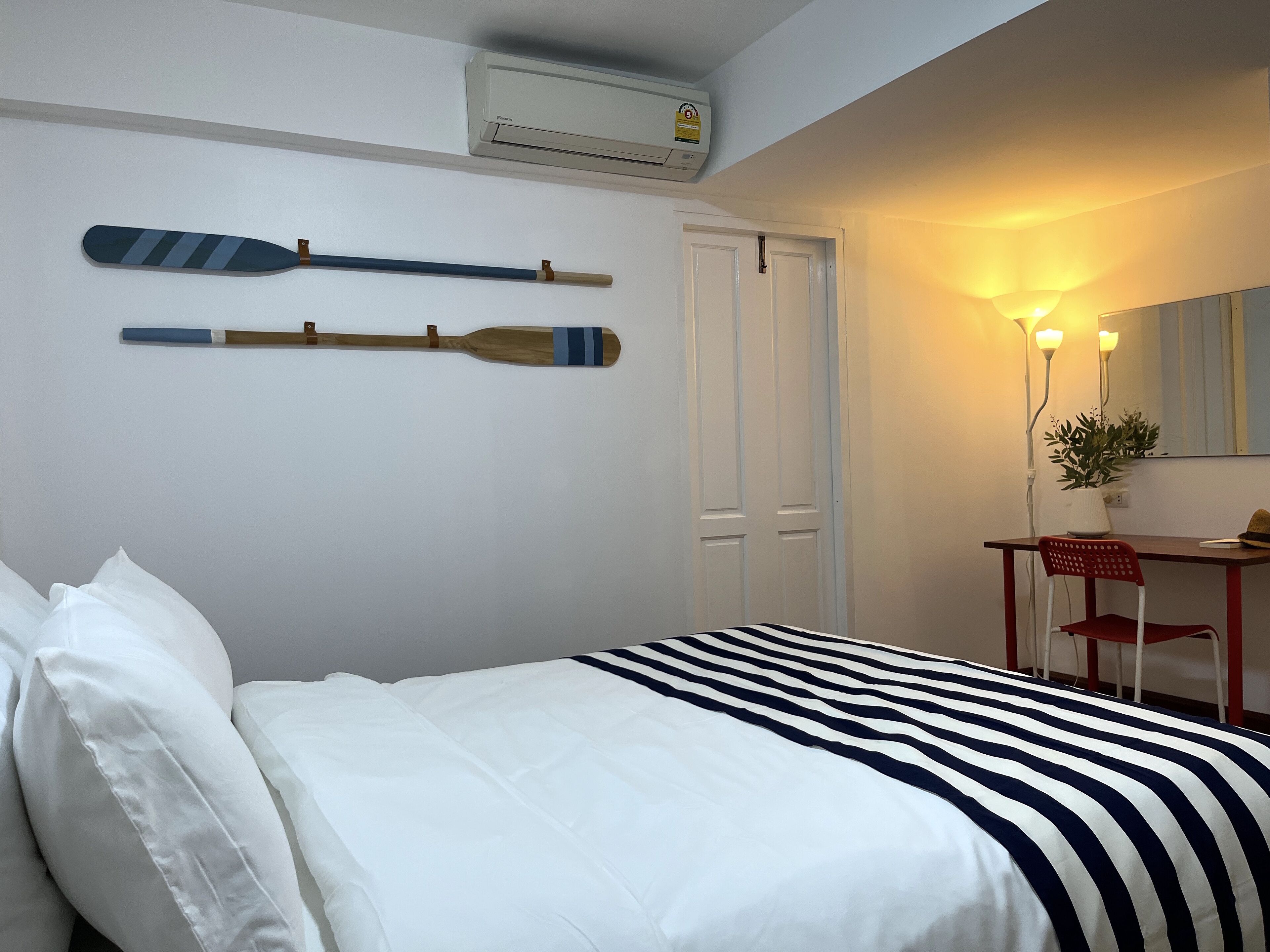 A bedroom with a bed, a desk, a chair, an air conditioning unit, and a door.