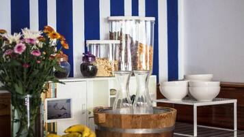 A room with a striped blue and white wall, a wooden barrel, a vase with flowers, a bowl of bananas, and a small table with bowls and a vase.