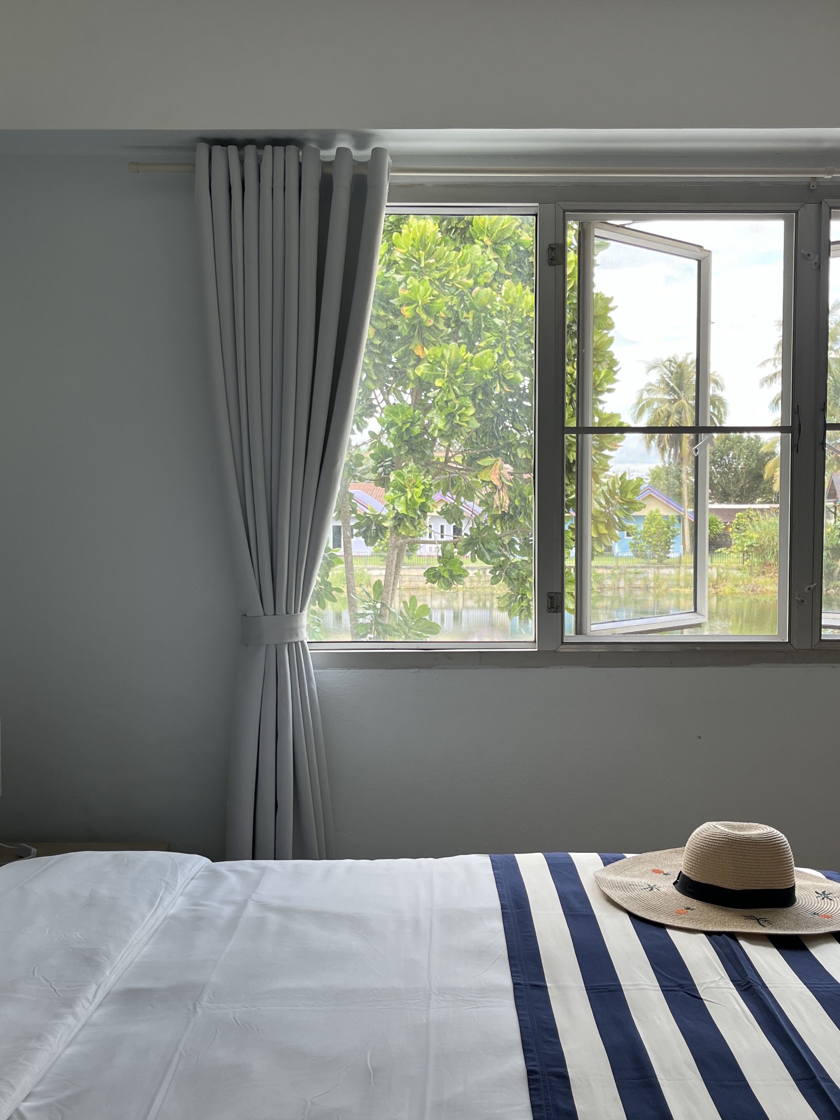 Une chambre avec un lit, une fenêtre avec des rideaux et un chapeau posé sur le lit.