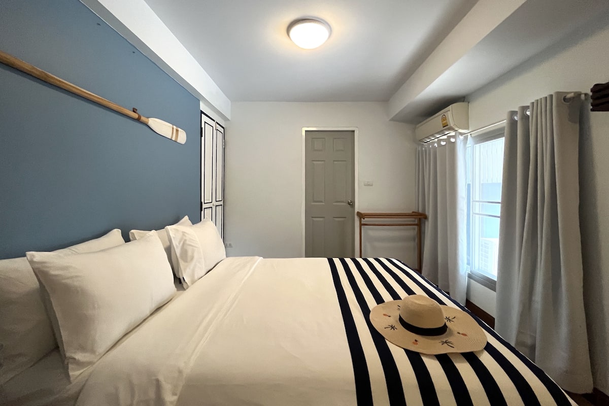 Habitación de hotel con cama, ventana con cortinas, puerta y lámpara fijada a la pared.