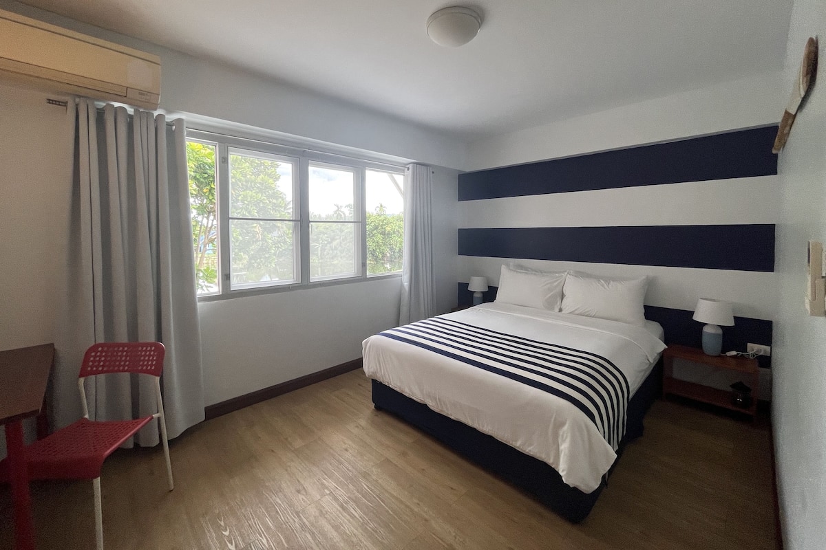 Habitación de hotel con cama, escritorio, silla y ventana con cortinas.