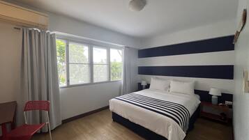 A hotel room with a bed, a desk, a chair, and a window with curtains.