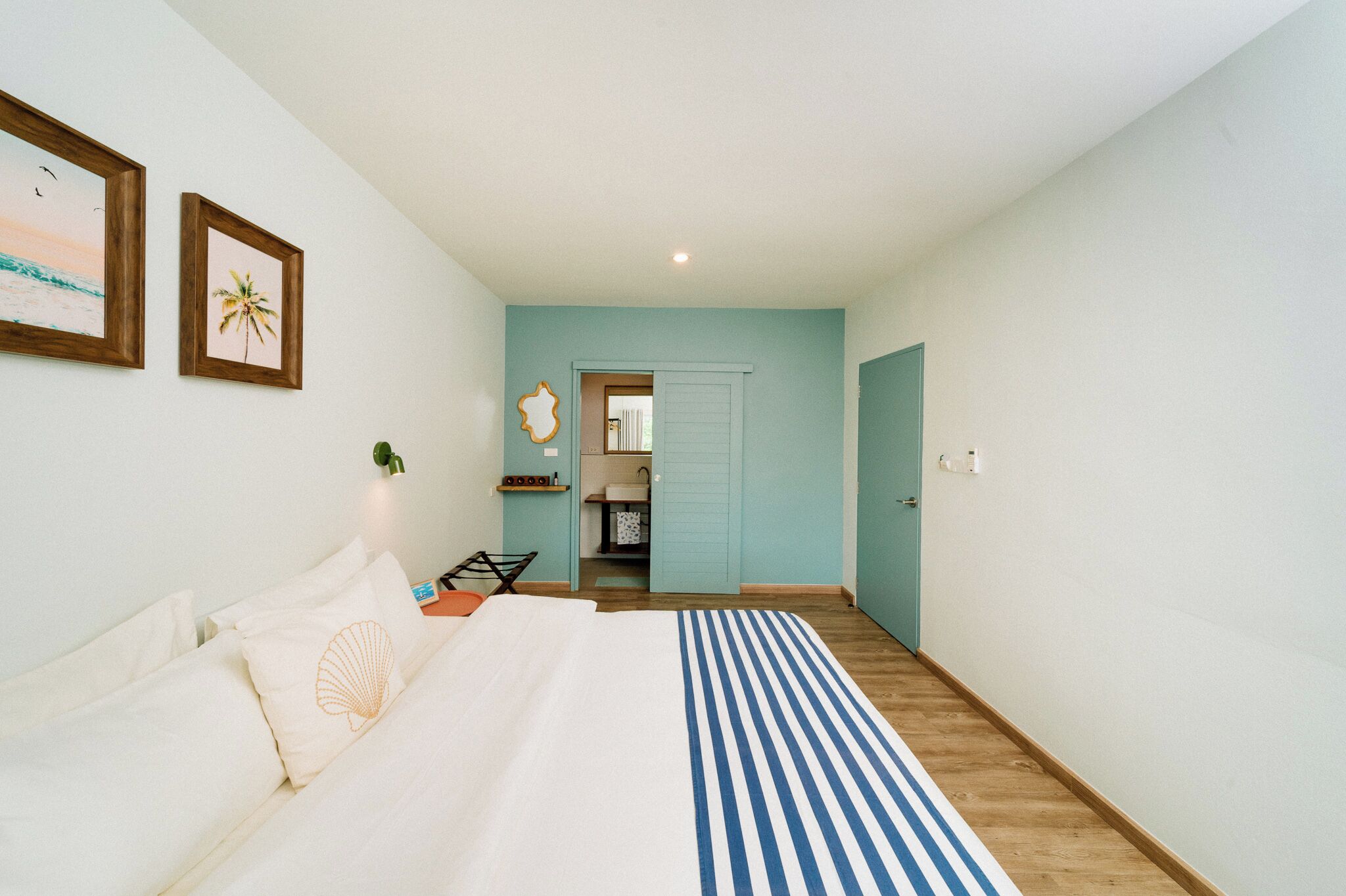 A bedroom with a bed, a nightstand, a lamp, and a view of a bathroom.