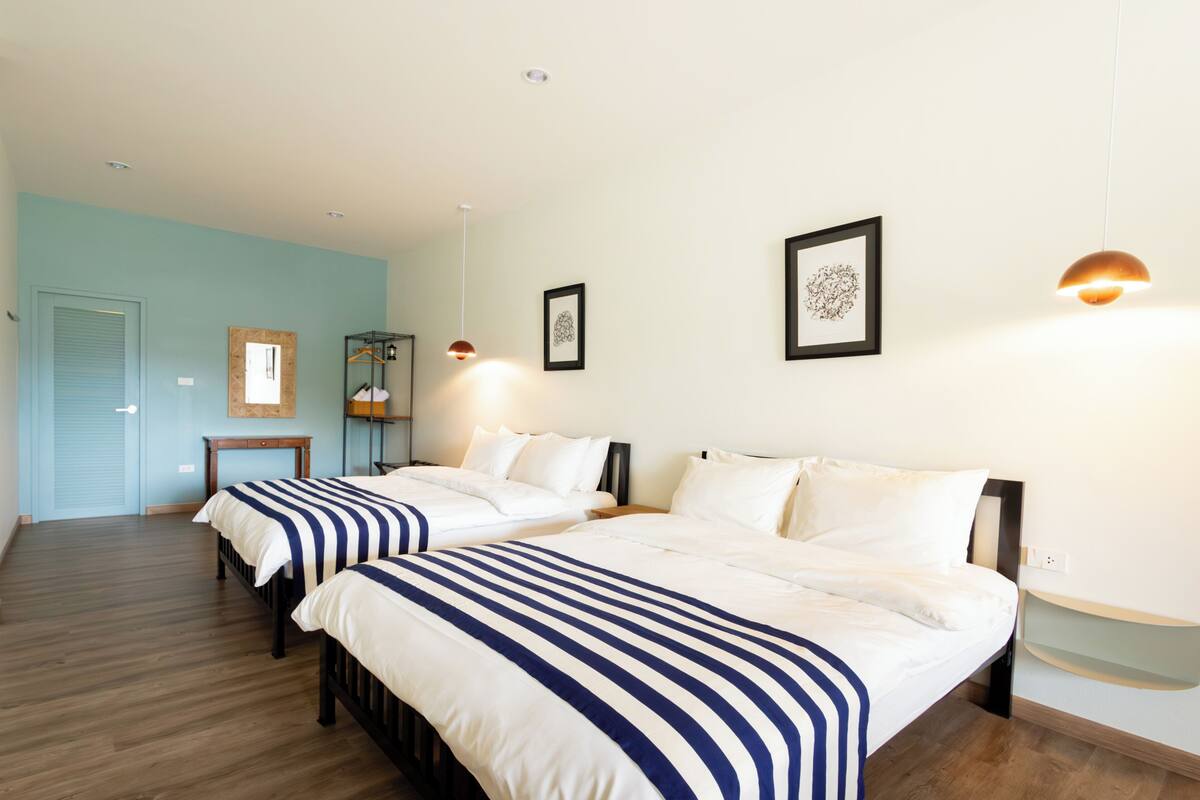 Habitación de hotel con dos camas, piso de madera, pared azul claro y una mesita con espejo.