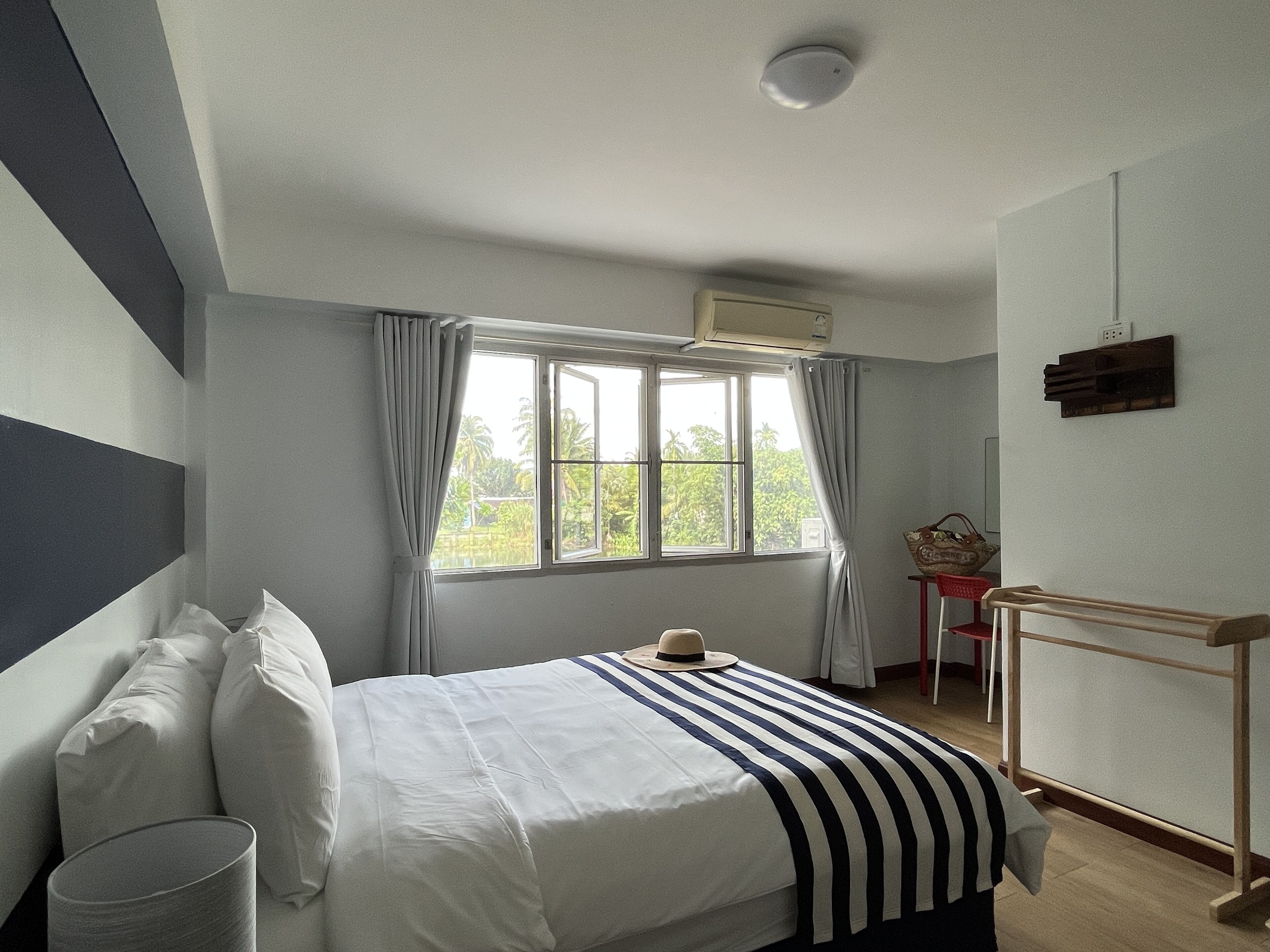 Ein Hotelzimmer mit Bett, einem Fenster mit Vorhängen, einem kleinen Tisch und einem an der Wand befestigten Regal.