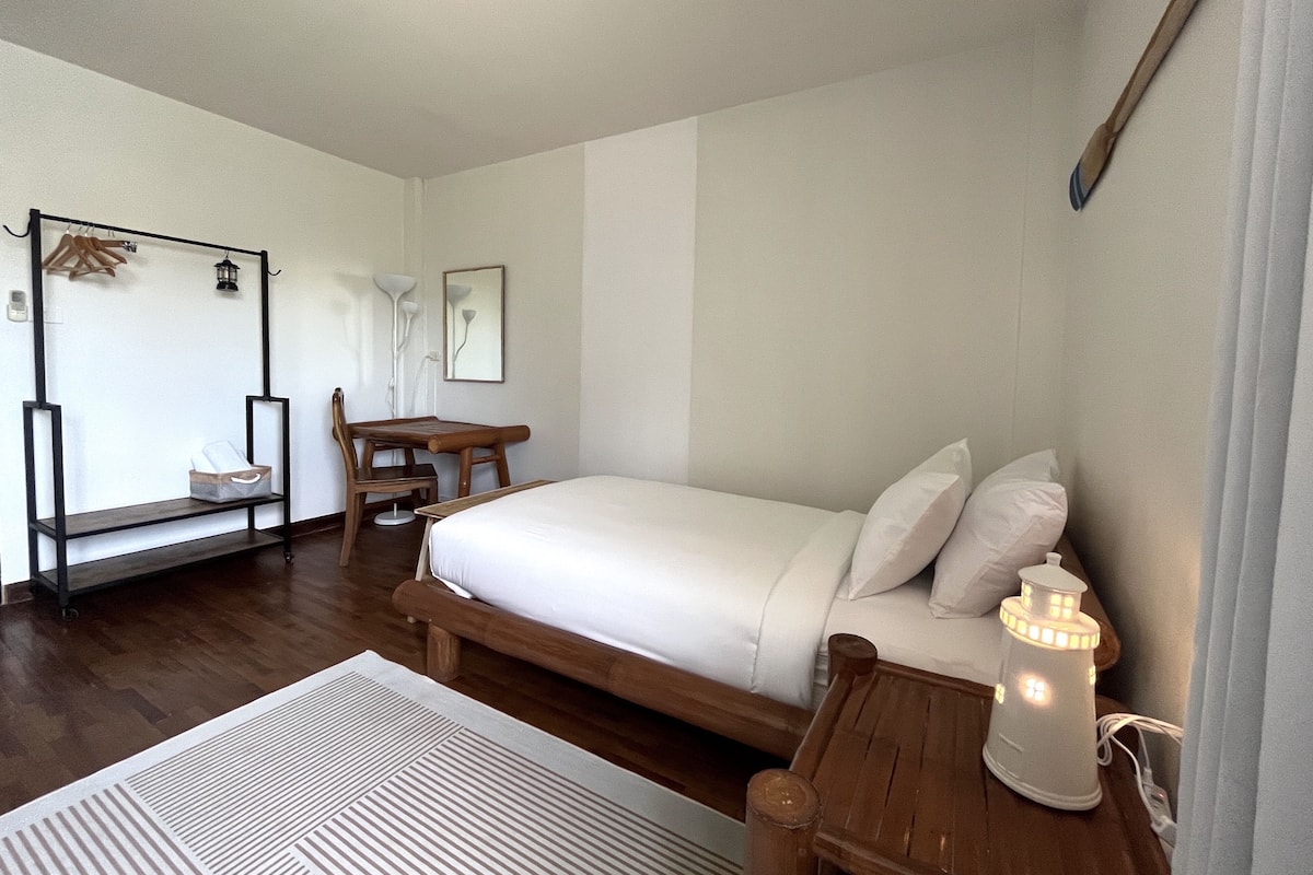 Un dormitorio con una cama de madera, un escritorio y una silla. Hay una lámpara colgante y una lámpara de pared.