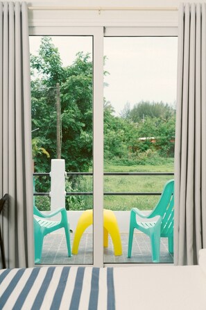 Une pièce dotée d’une porte-fenêtre coulissante donnant sur un espace extérieur aménagé avec des chaises et de la verdure.