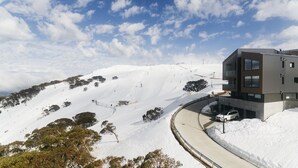 Un edificio moderno con una seggiovia sullo sfondo, circondato da colline innevate.