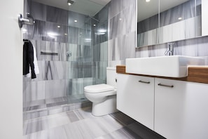 A modern bathroom with a glass shower enclosure, a white toilet, and a wooden vanity with a white sink.