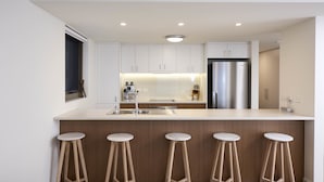 Una cucina moderna con mobili bianchi, un frigorifero in acciaio inossidabile e un angolo bar con sgabelli.