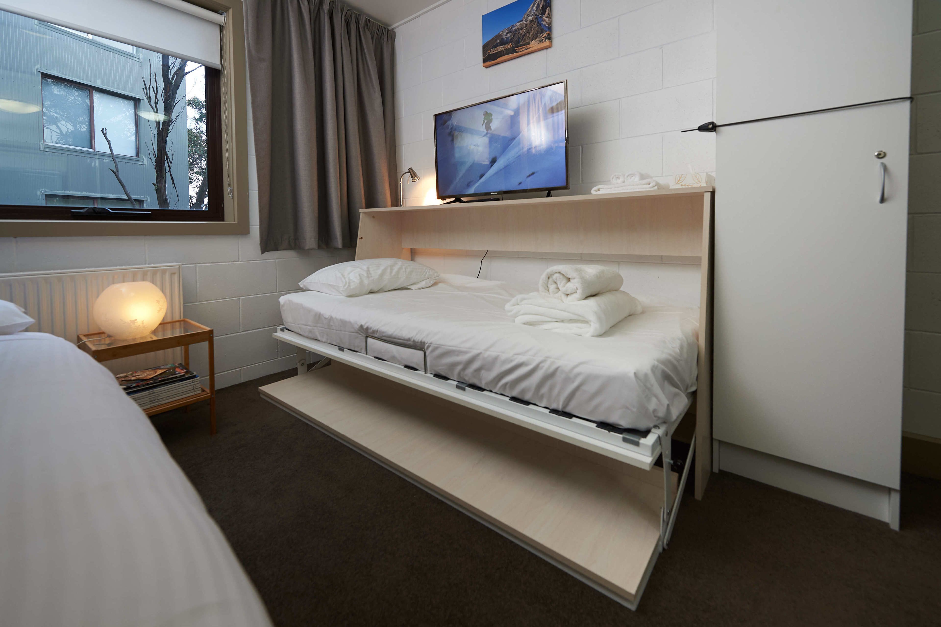 Une chambre d’hôtel comprenant un lit, une tél évision, une table de chevet avec une lampe et une armoire.