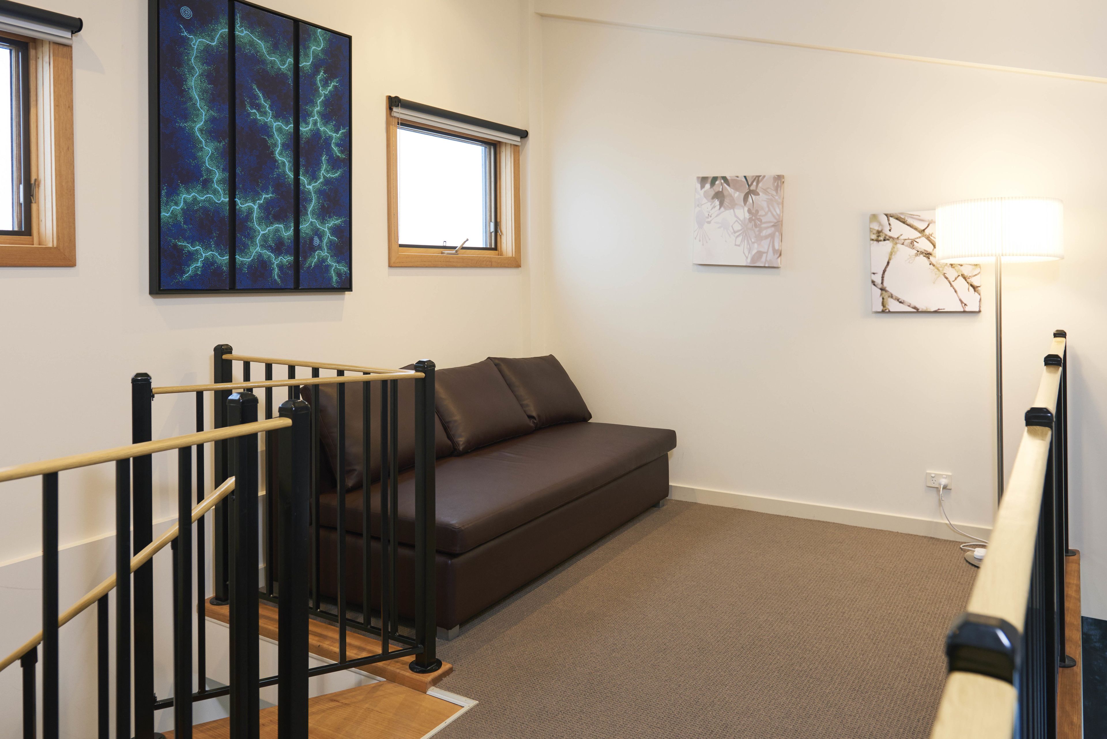 A modern living room with a brown sofa, a black railing, and artwork on the walls.