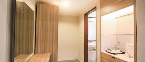 A modern hotel room with a wooden vanity, a mirror, a small table with toiletries, and a glass shower enclosure.