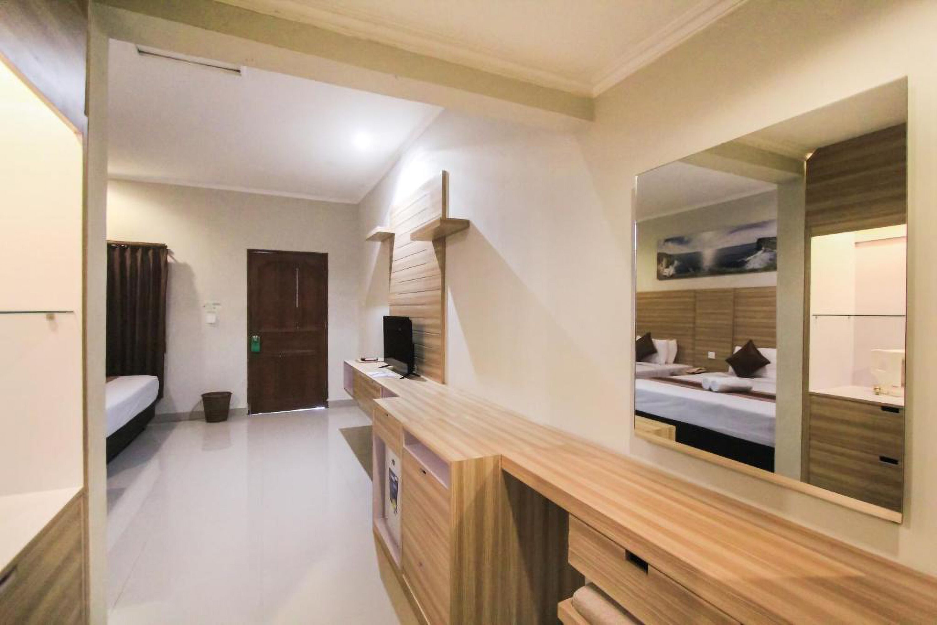 A hotel room with a wooden vanity, a large mirror, a bed, and a door.