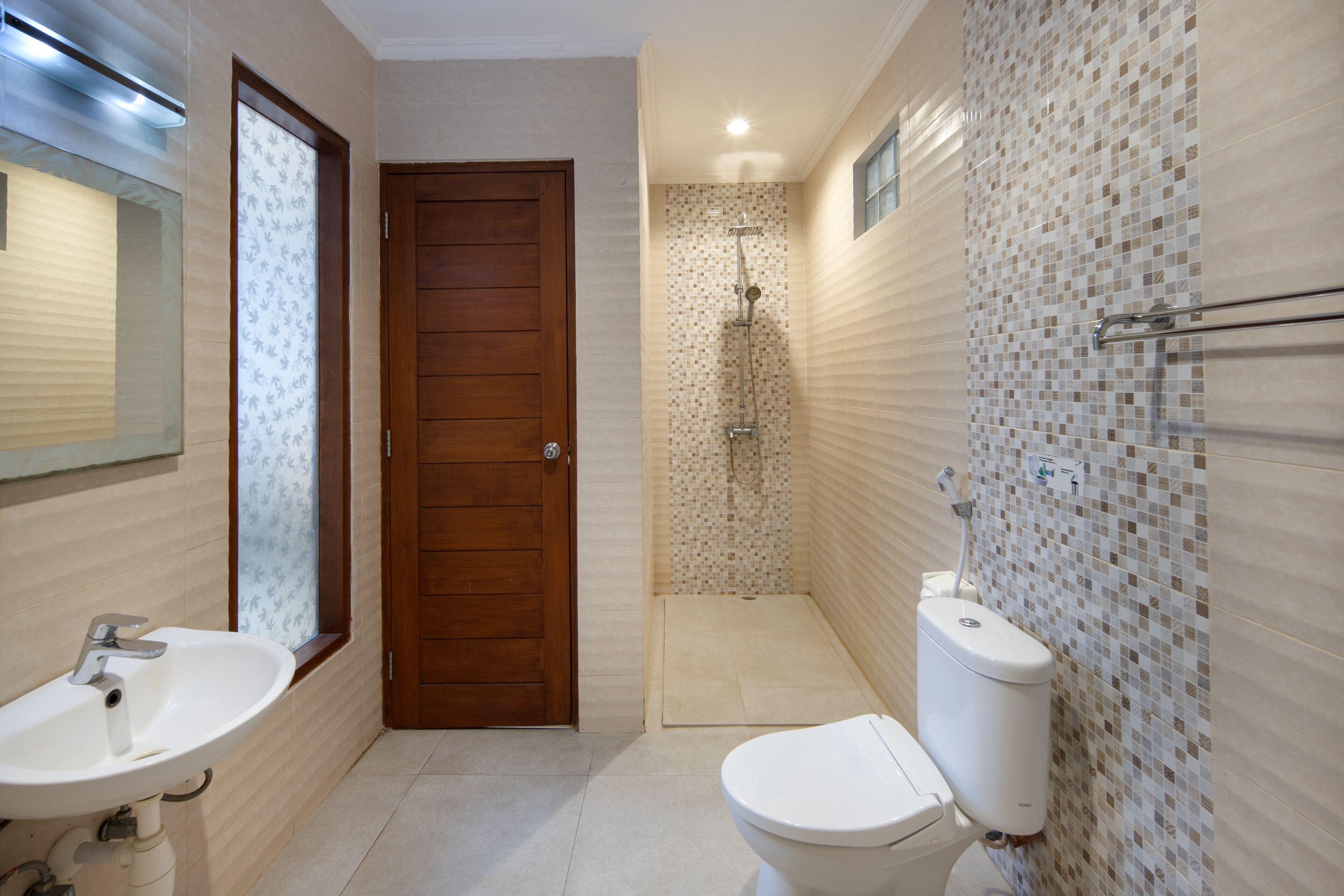 A bathroom with a wooden door, a white sink, a toilet, and a shower area.