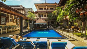 A pool area with lounge chairs and a building in the background. - Legian Village Beach Resort (Legian)