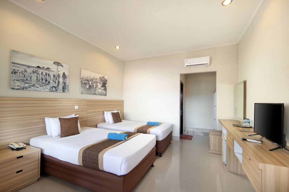 A hotel room with two beds, a desk with a TV, and artwork on the wall.