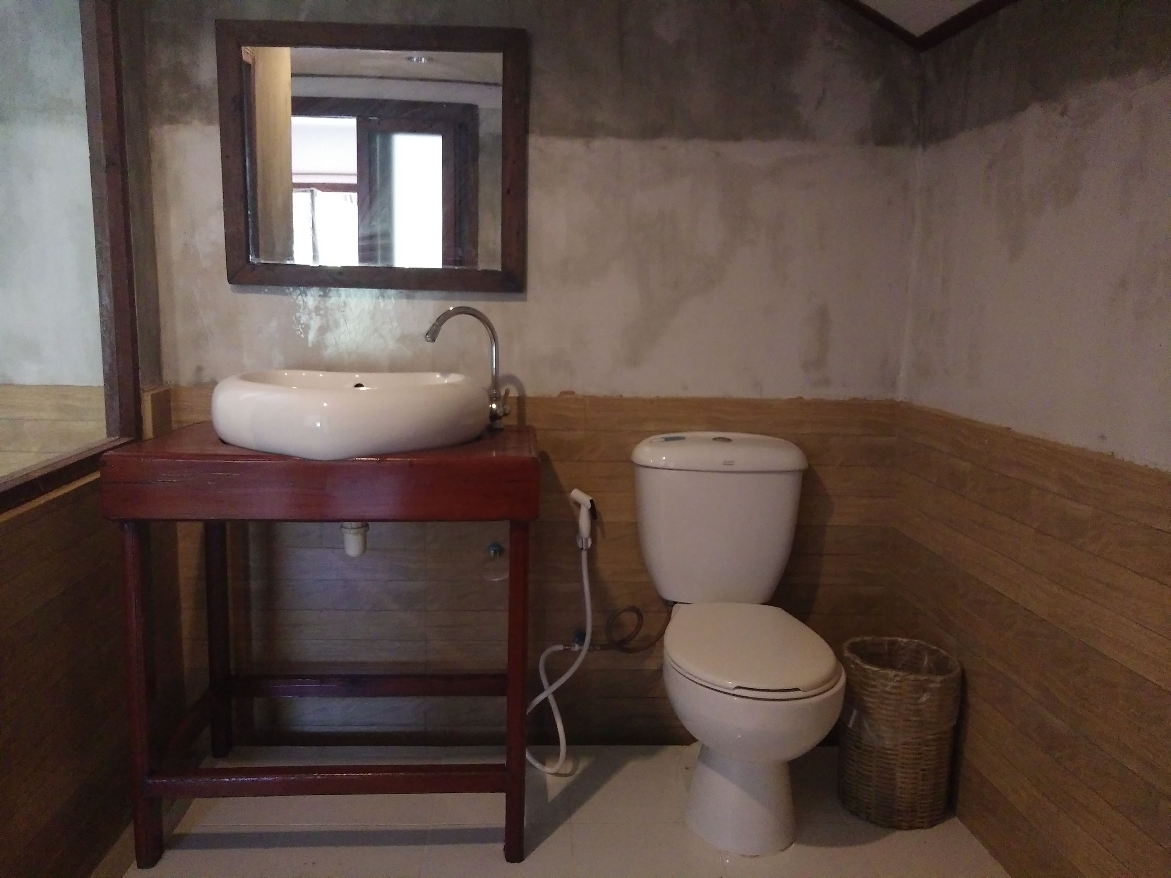 Un baño con tocador de madera, un lavabo blanco, un espejo, un inodoro y una cesta de mimbre.