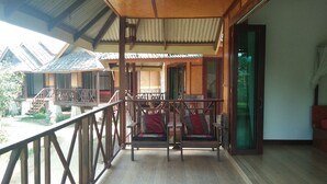 A wooden balcony with a railing, a wooden bench with cushions, and a view of other buildings. - Pai Park Cottage (Pai)