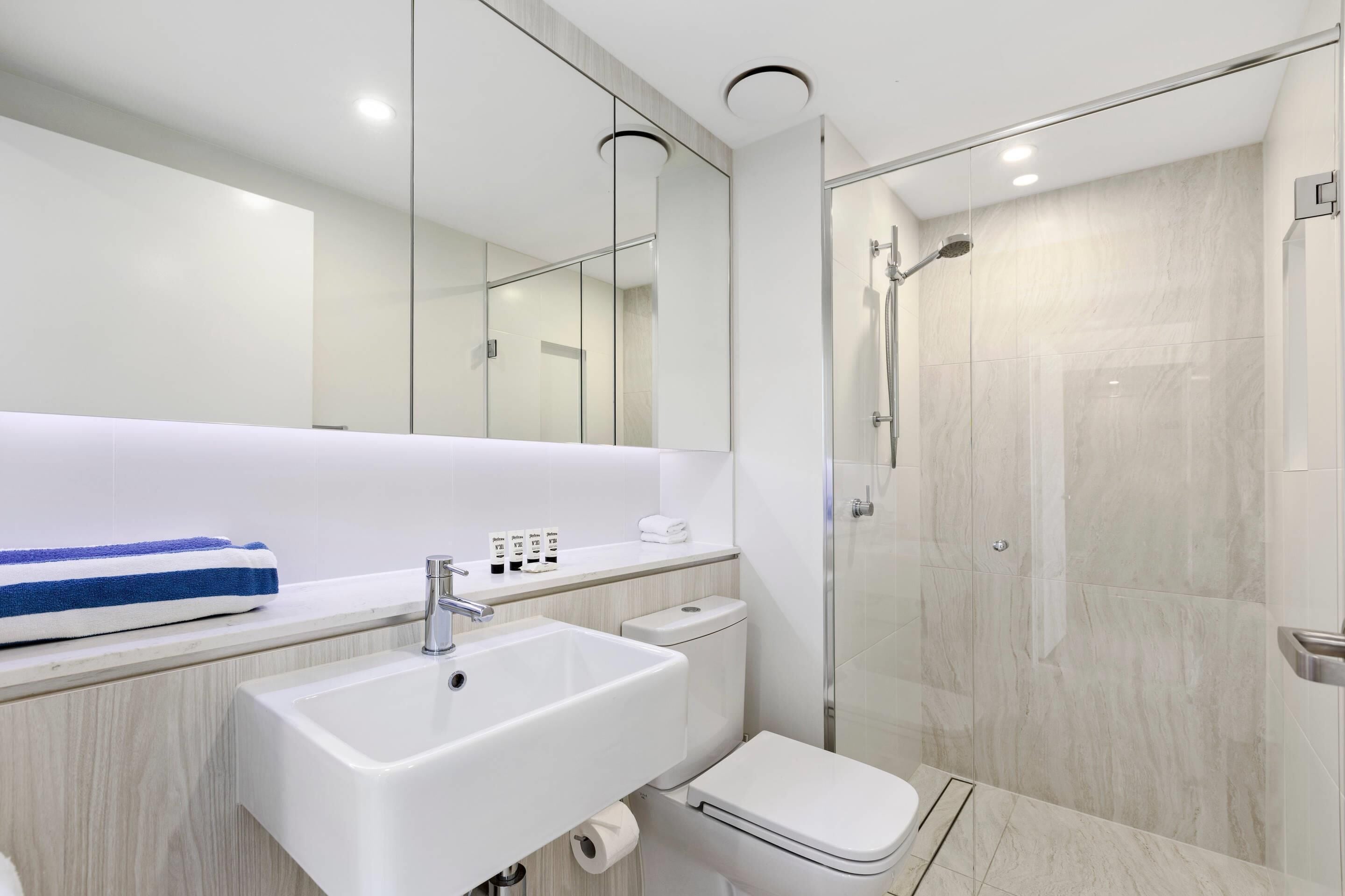 Un baño moderno con lavamanos blanco, inodoro y ducha con mampara de vidrio.