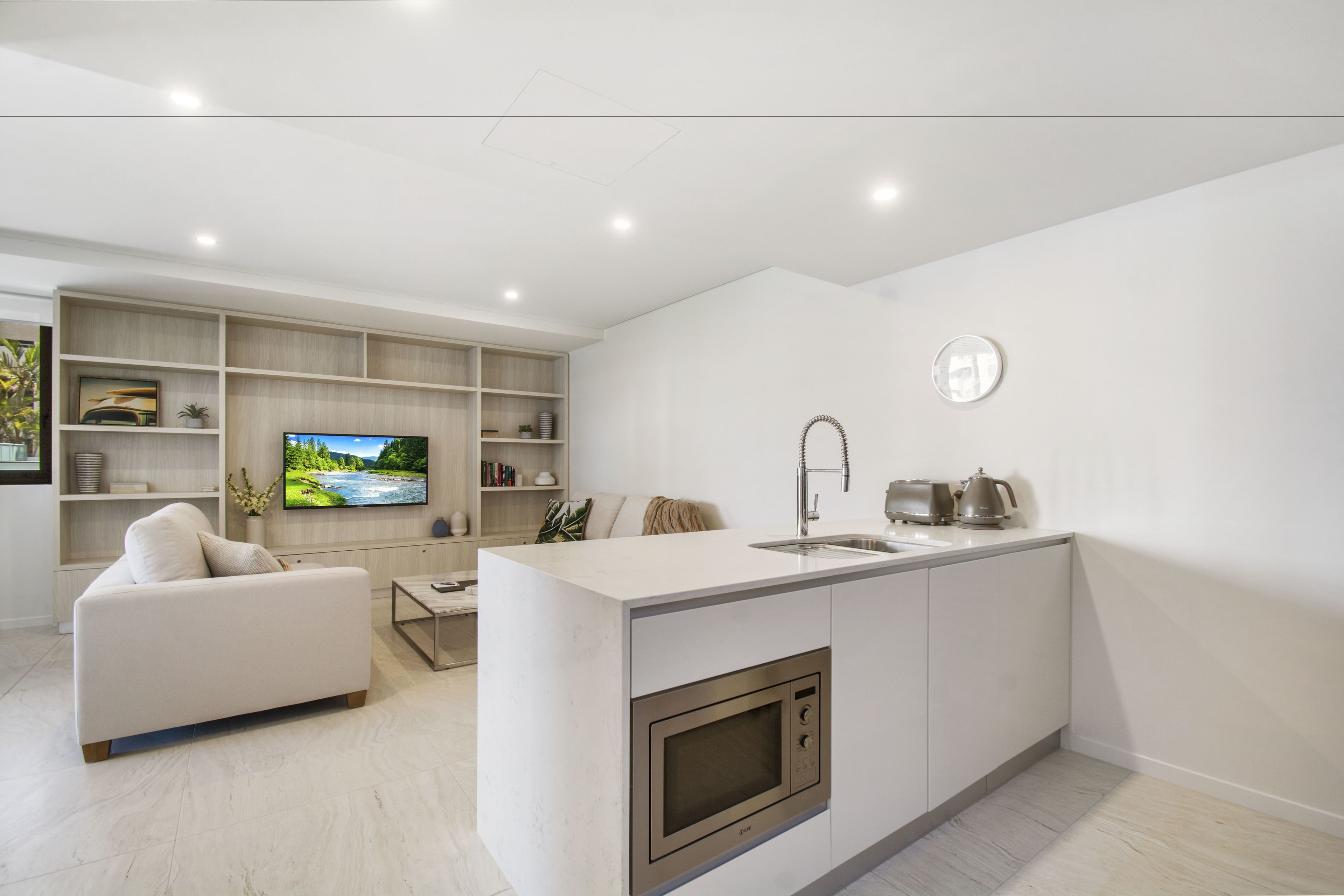 Una cocina moderna con horno empotrado, lavamanos y televisor. En la sala de estar, hay un sofá y una mesa de centro.