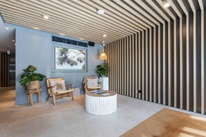 A modern lobby with a wooden ceiling, a round coffee table, two chairs, and potted plants. - Breeze Mooloolaba (Mooloolaba)