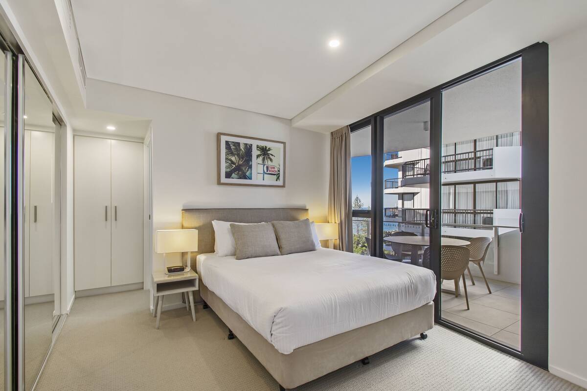 Une chambre d’hôtel moderne dotée d’un grand lit, d’une table de chevet, d’un bureau et d’un balcon avec une table et des chaises.