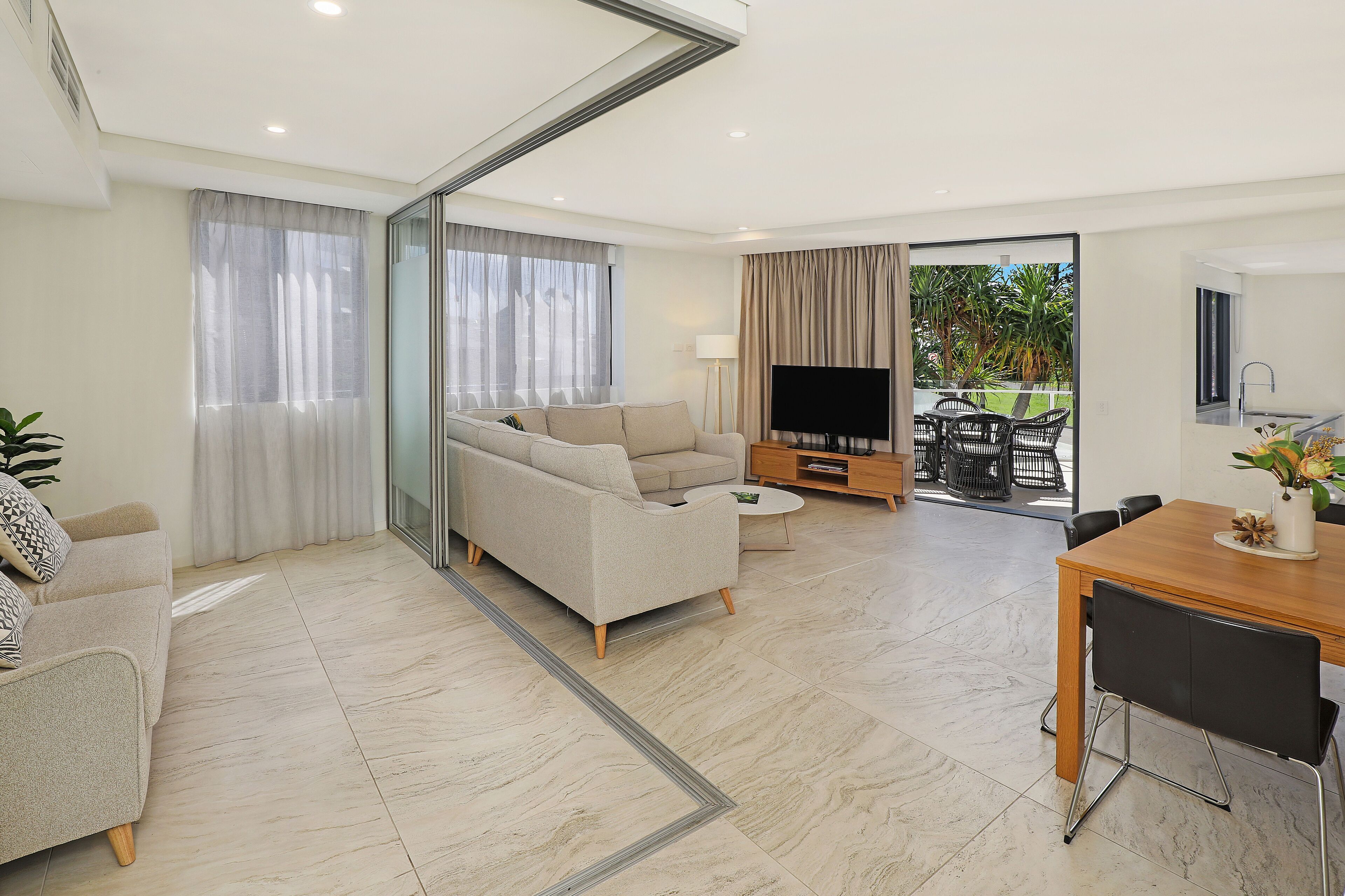 A modern living room with a sofa, a coffee table, and a TV. There is a dining area with a table and chairs.
