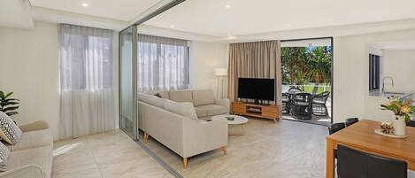 A modern living room with a sofa, a coffee table, and a TV. There is a dining area with a table and chairs.