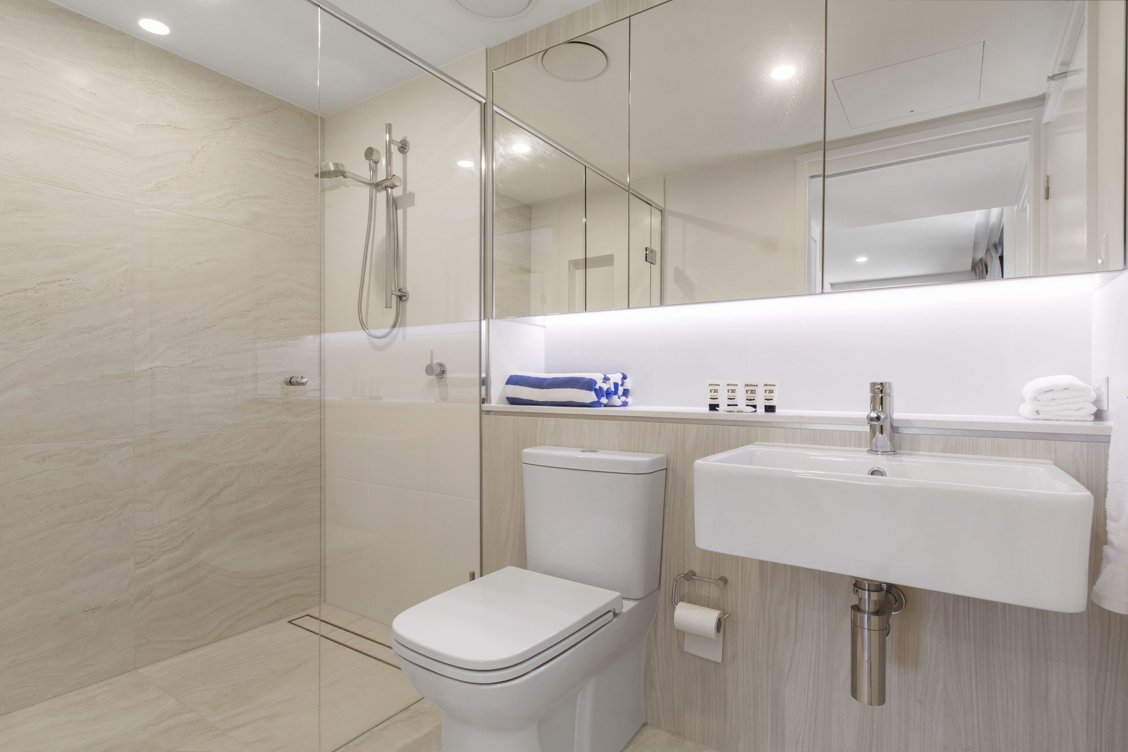 A modern bathroom with a glass-enclosed shower, a toilet, and a sink with a mirror above it.