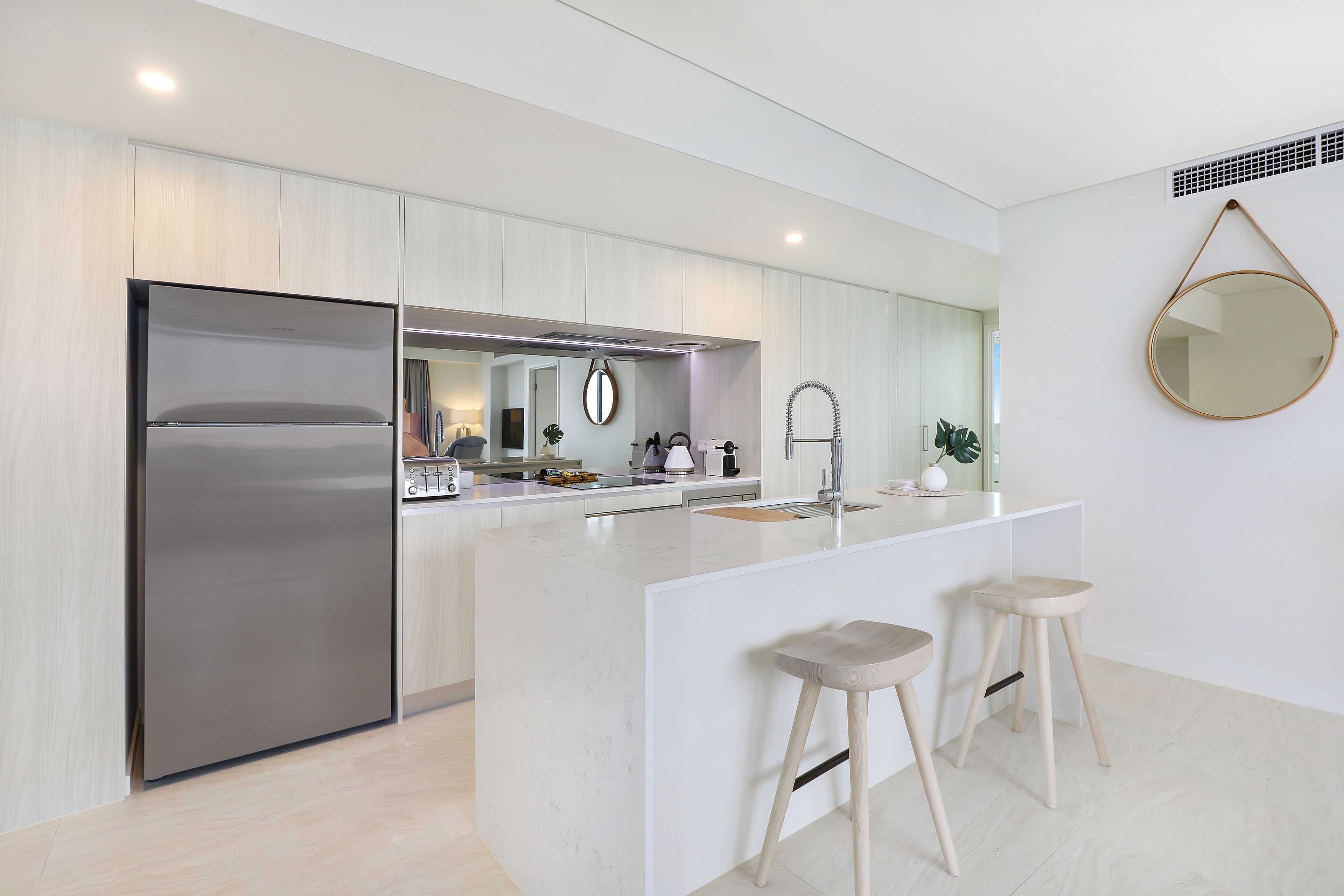 A modern kitchen with a large island, stainless steel refrigerator, and wooden stools.