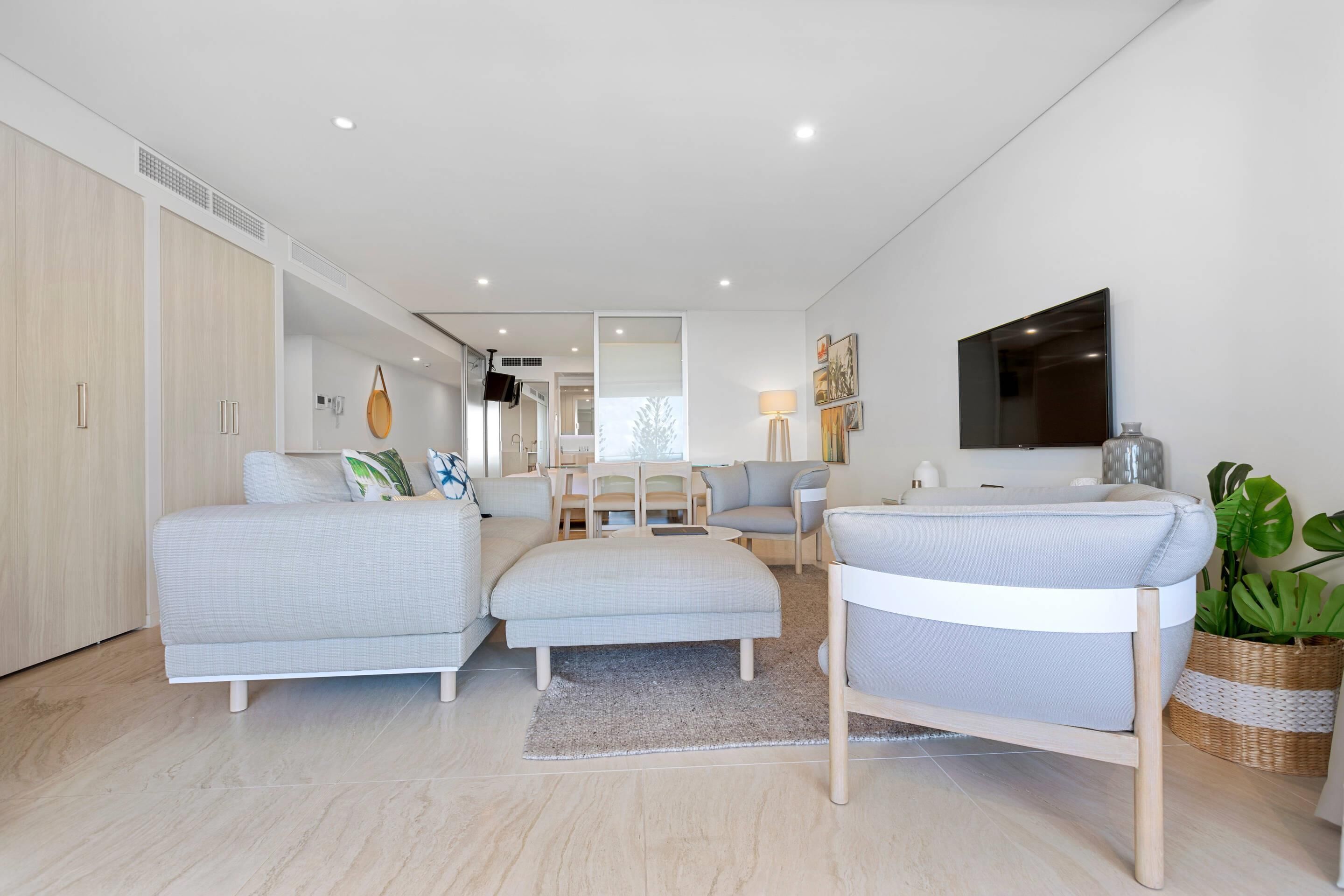 A modern living room with a sofa, ottoman, and a TV mounted on the wall.