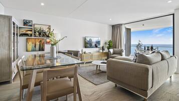 Uma sala de estar moderna com uma mesa de jantar de vidro, sofá bege e vista para o mar.