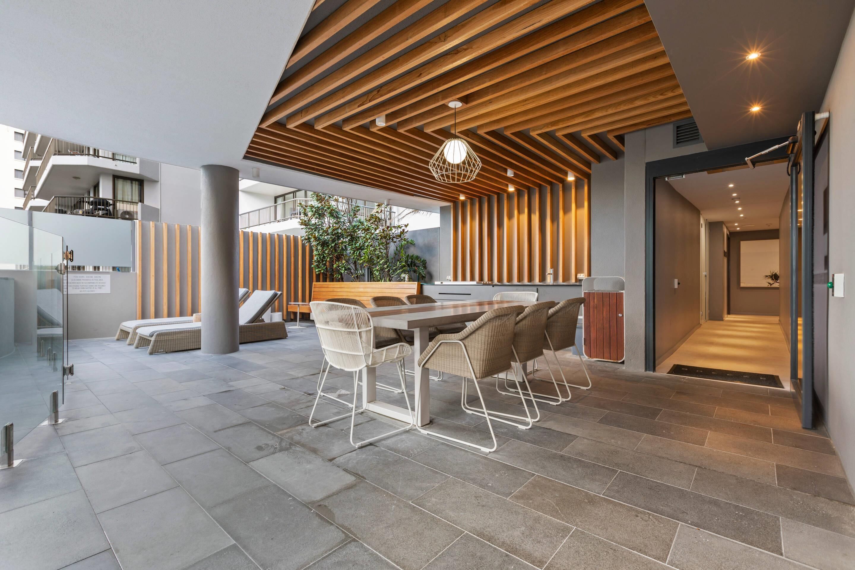 Espaço interno moderno com teto de madeira, área de refeições com mesa e cadeiras, e vista para uma varanda com plantas.