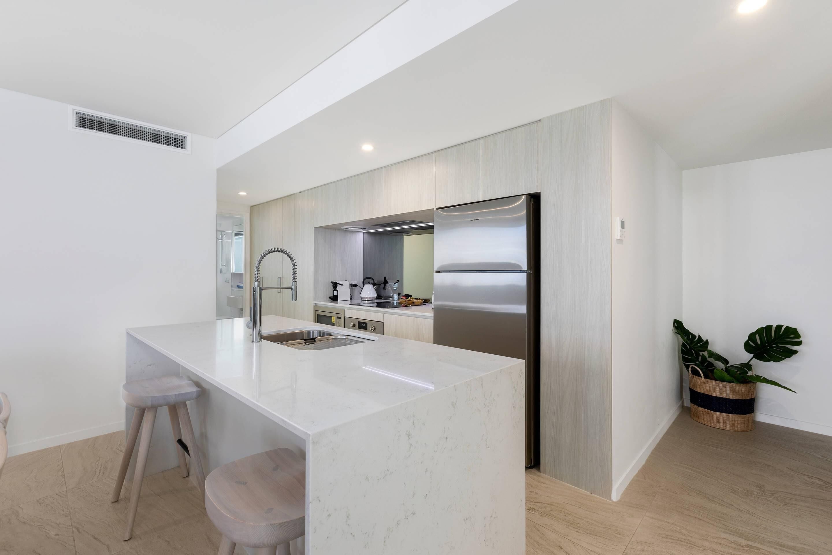 Une cuisine moderne dotée d’un îlot central, d’appareils électroménagers en acier inoxydable et d’un plancher en bois.