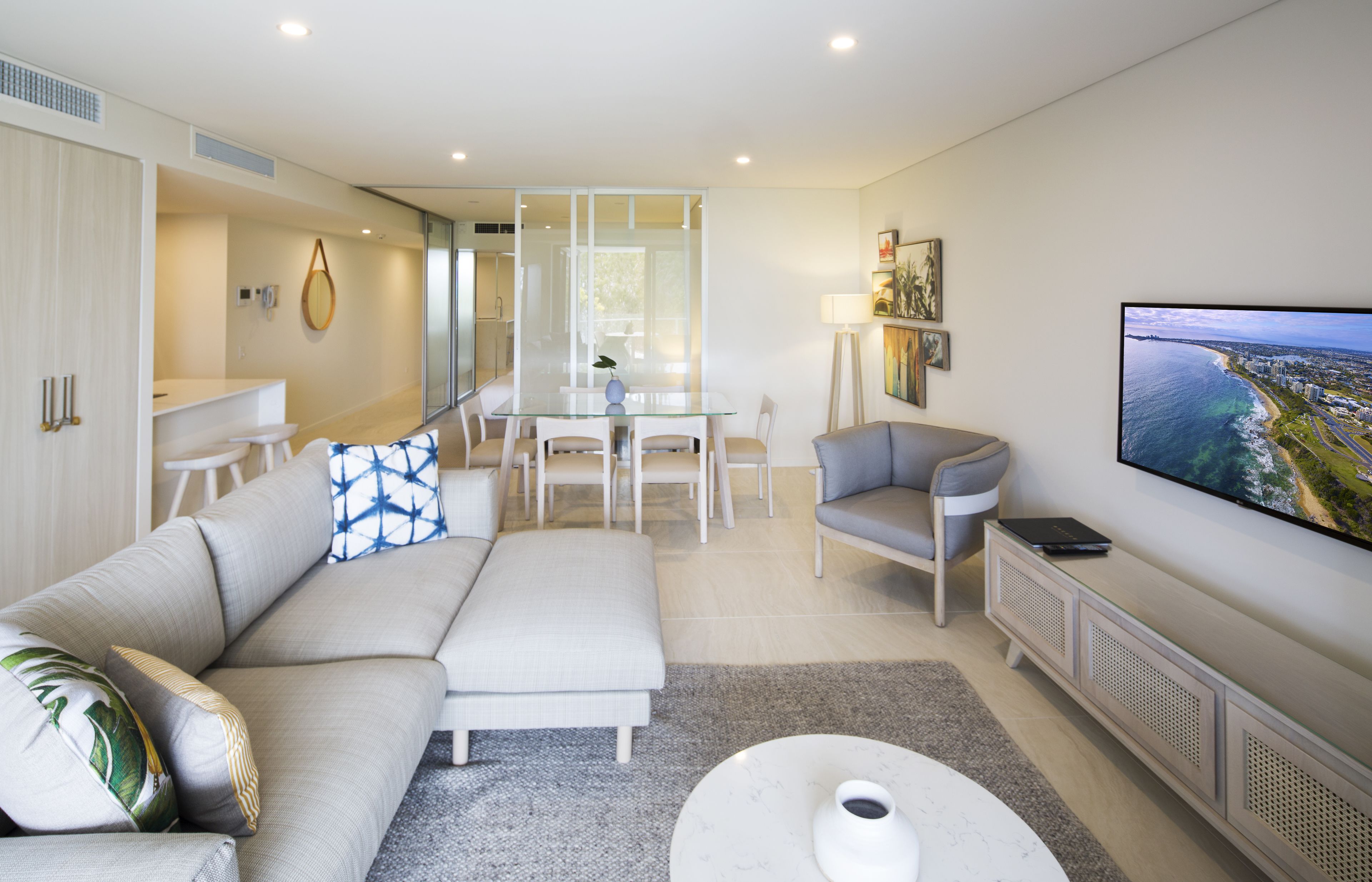 Una sala de estar moderna con un sofá, una mesa de centro, un televisor y un comedor con una mesa de vidrio y sillas.