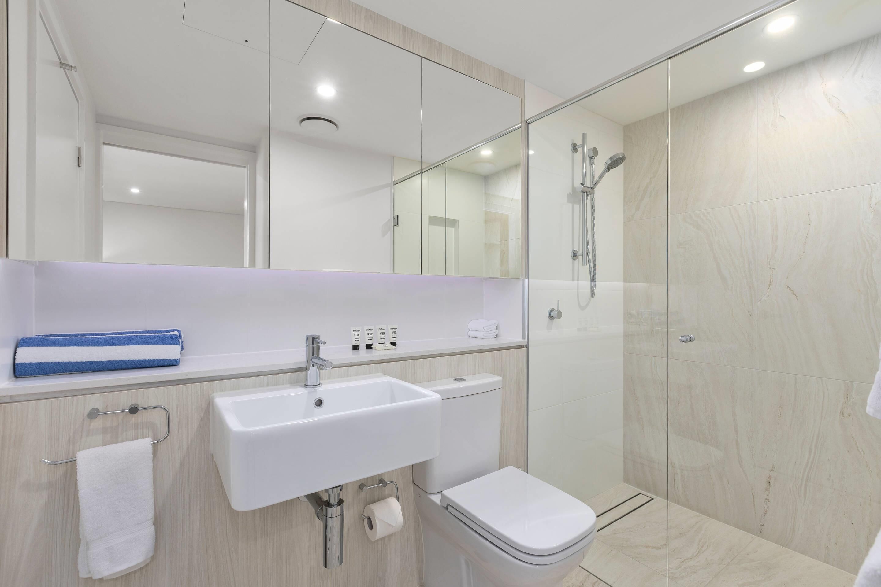 Un baño moderno con lavamanos blanco, inodoro y cabina de ducha con mampara de vidrio.