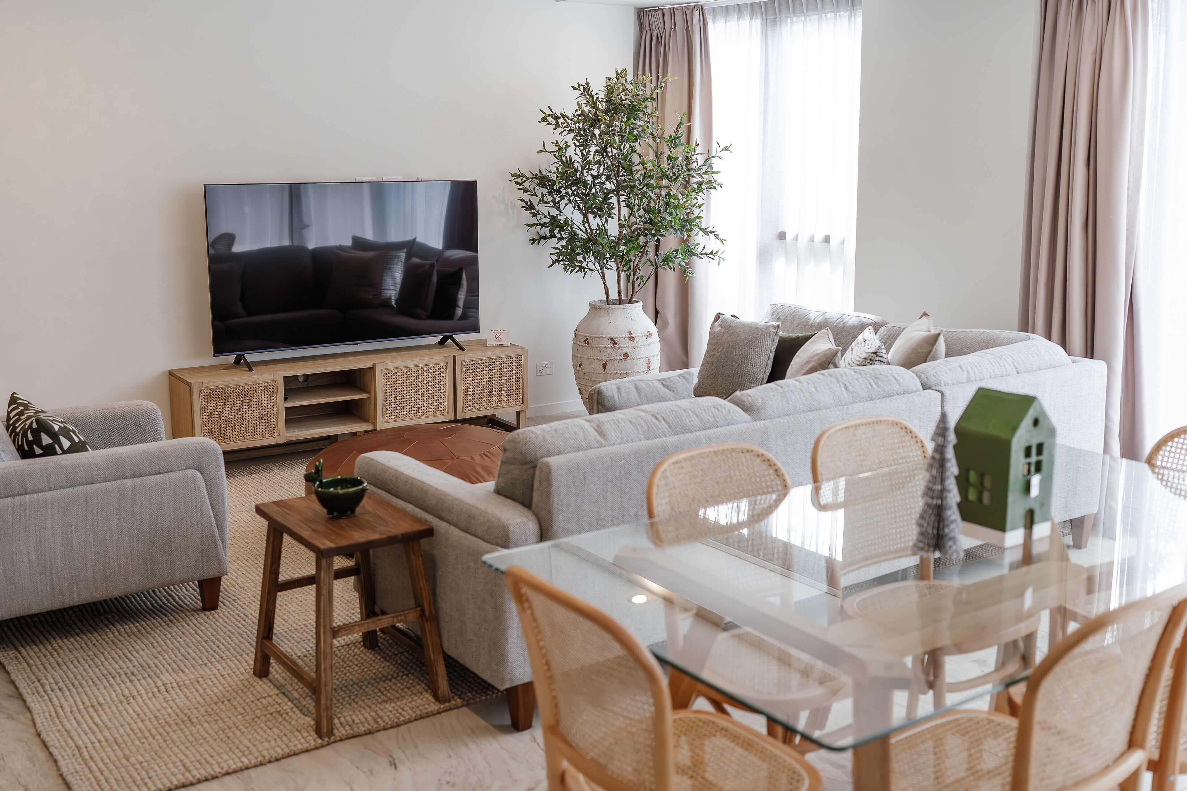 A modern living room with a flat-screen TV, a sofa set, a dining table with chairs, and a decorative house model.
