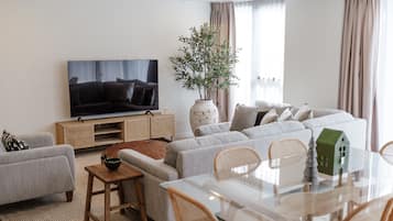 A modern living room with a flat-screen TV, a sofa set, a dining table with chairs, and a decorative house model.