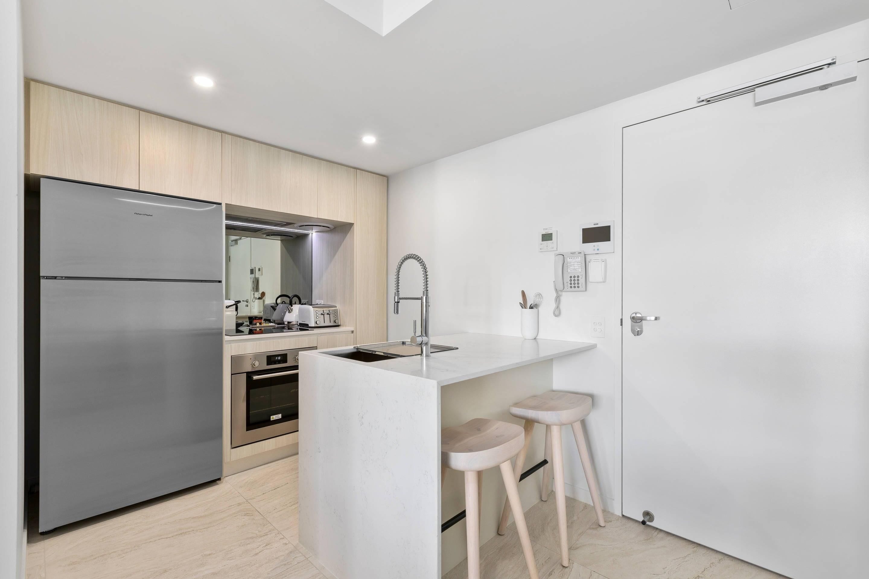 A modern kitchen with a built-in refrigerator, oven, and sink, wooden cabinets, and a white countertop.