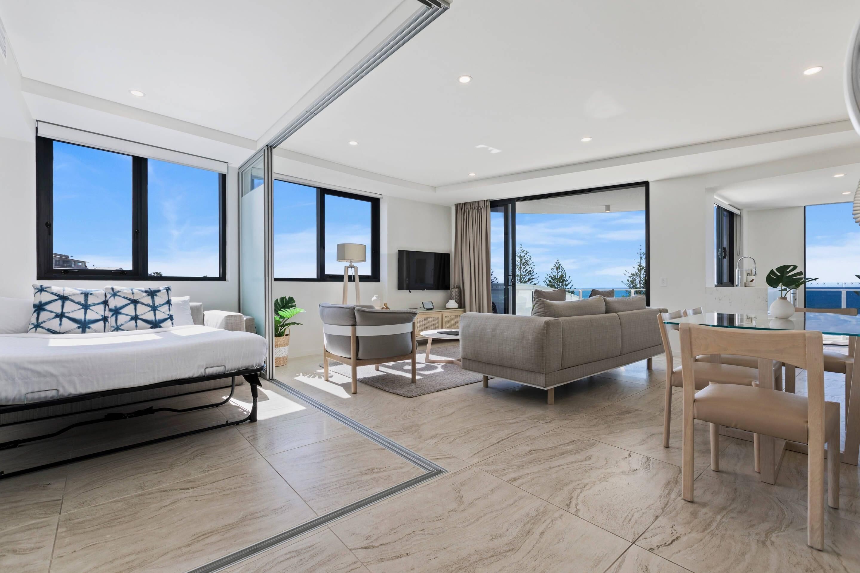 Una habitación de hotel moderna con cama, sofá, mesa de comedor y ventanas amplias.