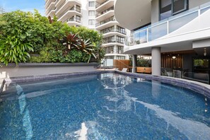 A swimming pool with a tiled edge, surrounded by greenery and a modern building with balconies. - Breeze Mooloolaba (Mooloolaba)