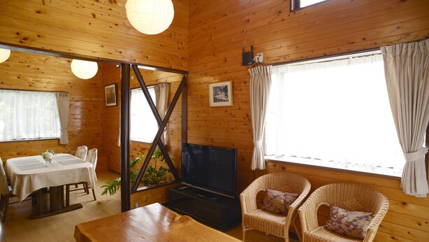 A wooden cabin interior with a dining table, chairs, a TV, and wicker furniture. - Kawaguchiko country cottage Ban (Fujikawaguchiko)