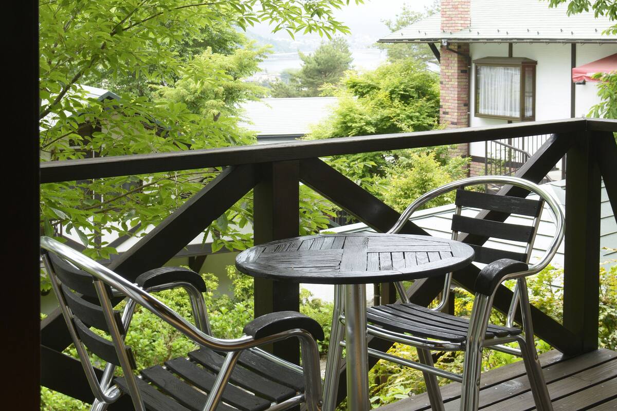 A wooden deck with metal chairs and a table, overlooking a body of water and greenery.