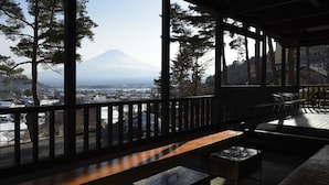 A wooden deck with a bench and a grill, overlooking a snowy landscape and a mountain. - Kawaguchiko country cottage Ban (Fujikawaguchiko)