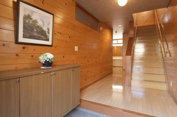 Interior de madera con una escalera, un cuadro en la pared y un mueble con un jarrón de flores.