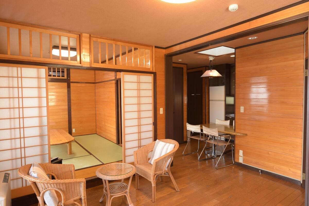 A traditional Japanese room with tatami flooring, low wooden partitions, and a dining area with a table and chairs.